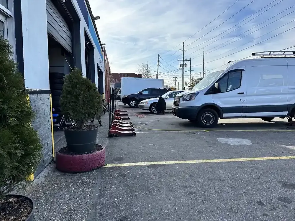 White van parked beside an open tire bay and potted shrub outside the shop